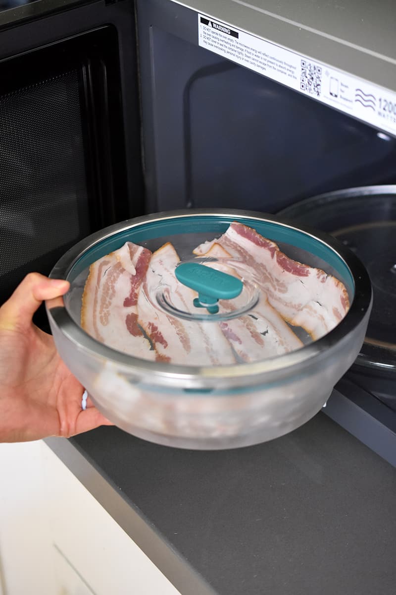Placing a closed container of raw bacon into an open microwave
