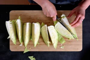 An overhead shot of someone cutting up a green cabbage into 8 wedges on a wooden cutting board