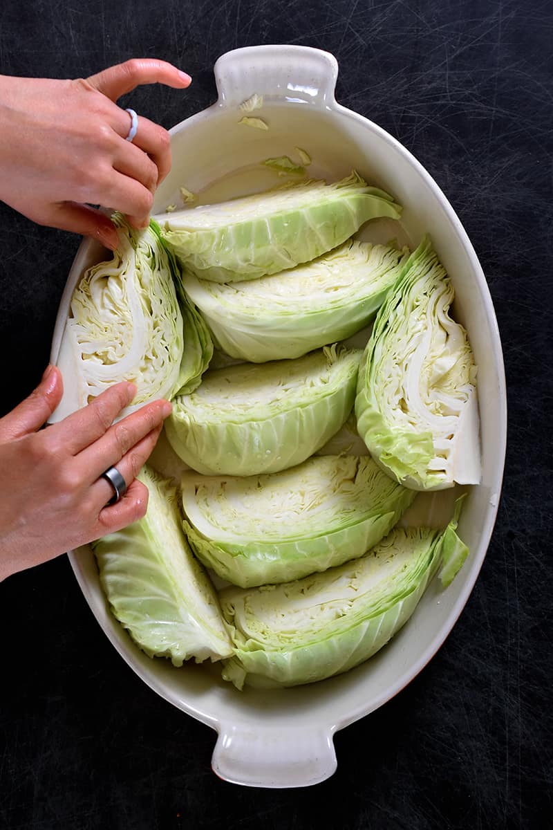 Overhead shot of someone arranging green cabbage wedges in an oval casserole pan.