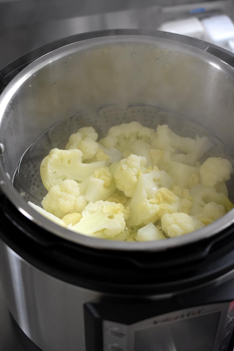 An open Instant Pot with steamed cauliflower florets and sliced garlic inside.
