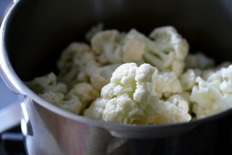 Closeup shot of cauliflower florets and sliced garlic in a pot.
