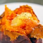 Close up of a baked sweet potato topped with melted ghee, salt, and pepper.