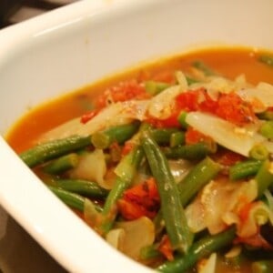 A bowl of paleo braised green beans with tomatoes and onions.