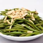 A plate of microwaved green beans in a white bowl topped with slivered almonds.