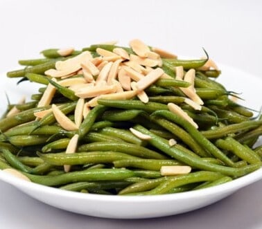 A plate of microwaved green beans in a white bowl topped with slivered almonds.