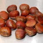 A pile of raw chestnuts sitting on a metal countertop.