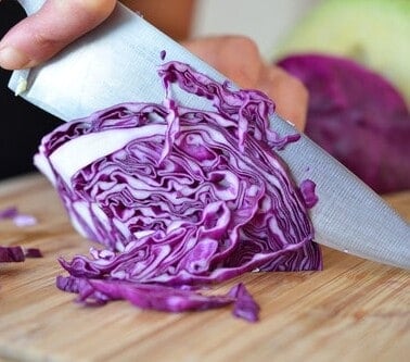Someone slicing a red cabbage on a cutting board for paleo sautéed red cabbage with onions, garlic, and anchovy.