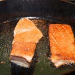 Two sous vide cooked pork bellies frying on a cast iron skillet.