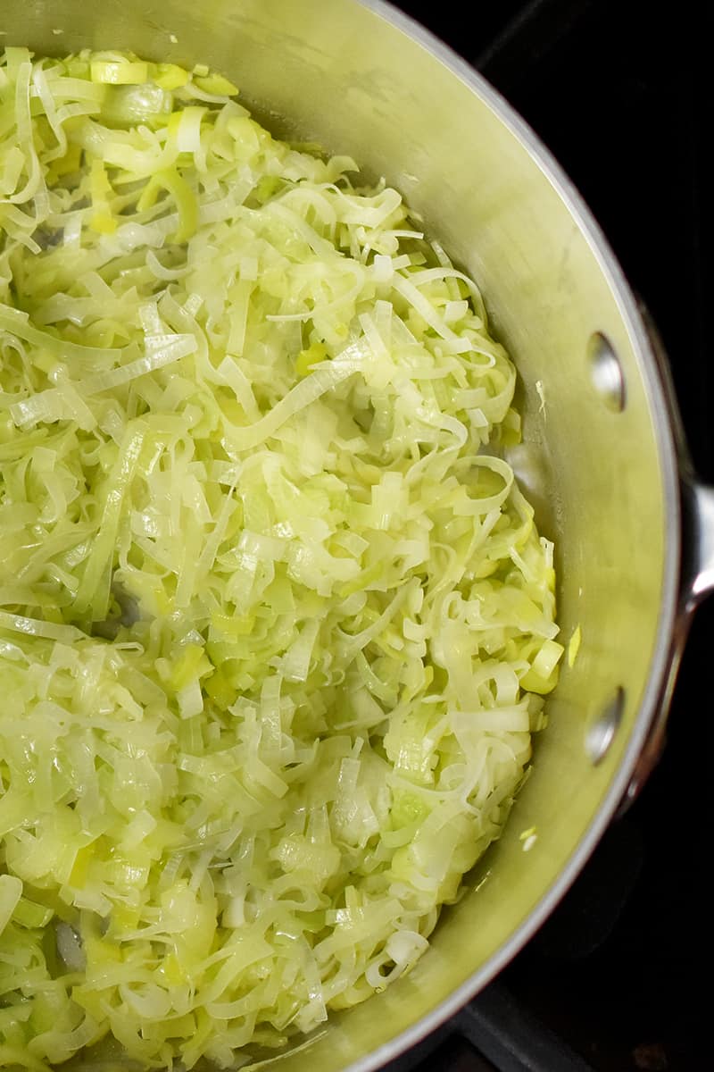 An overhead shot of softened sliced leeks in a large saucepan