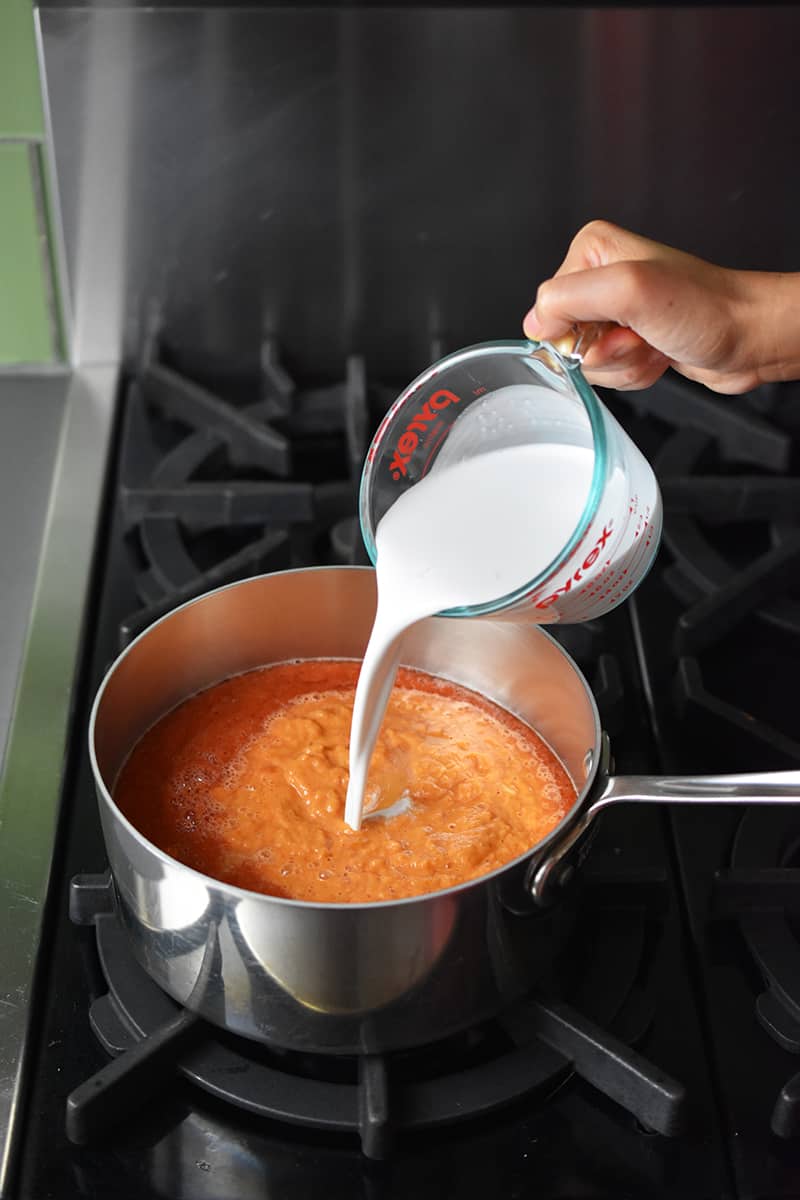 Pouring coconut milk into a saucepan of tomato soup