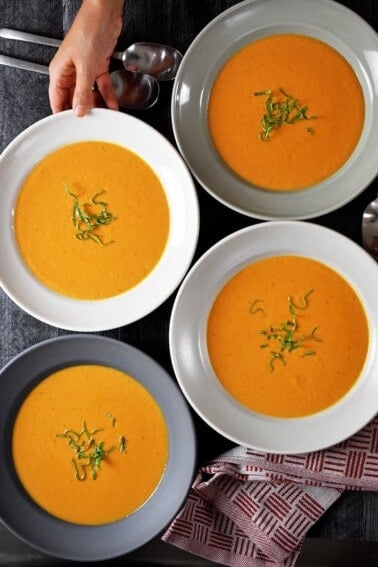 An overhead shot of four bowls filled with Whole30-friendly, paleo, and dairy-free Cream of Tomato Soup topped with basil