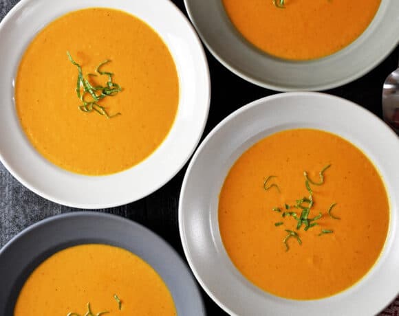 An overhead shot of four bowls filled with Whole30-friendly, paleo, and dairy-free Cream of Tomato Soup topped with basil
