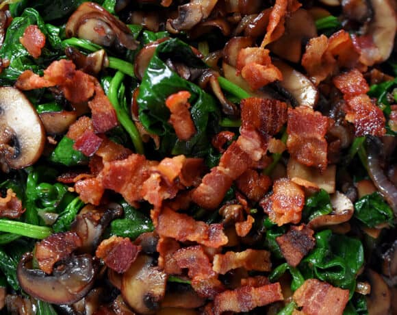 An overhead shot of a plate filled with sautéed spinach, crispy bacon bits, shallots, and mushrooms.