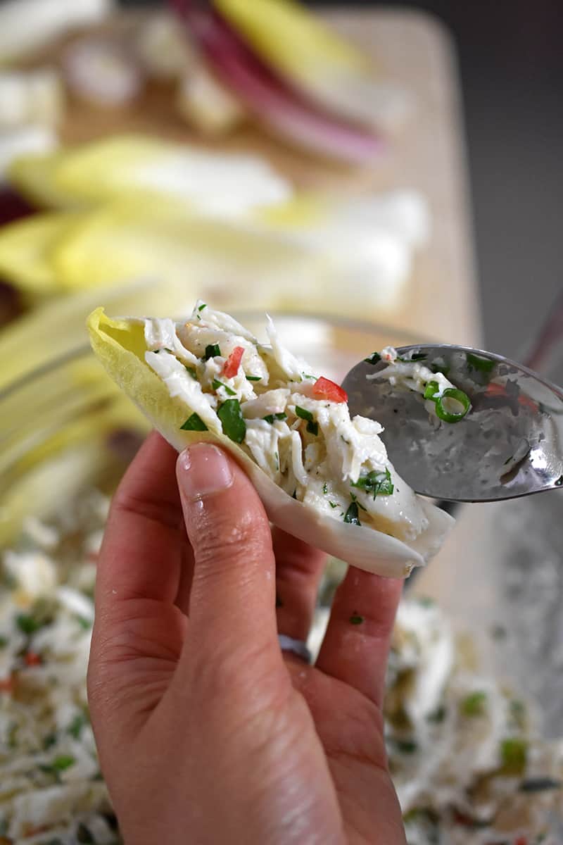 Someone spooning crab salad into an endive spear.