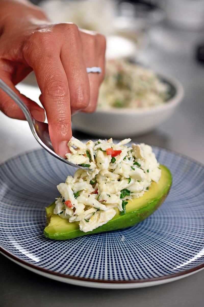 Spooning crab salad onto a halved and peeled avocado.