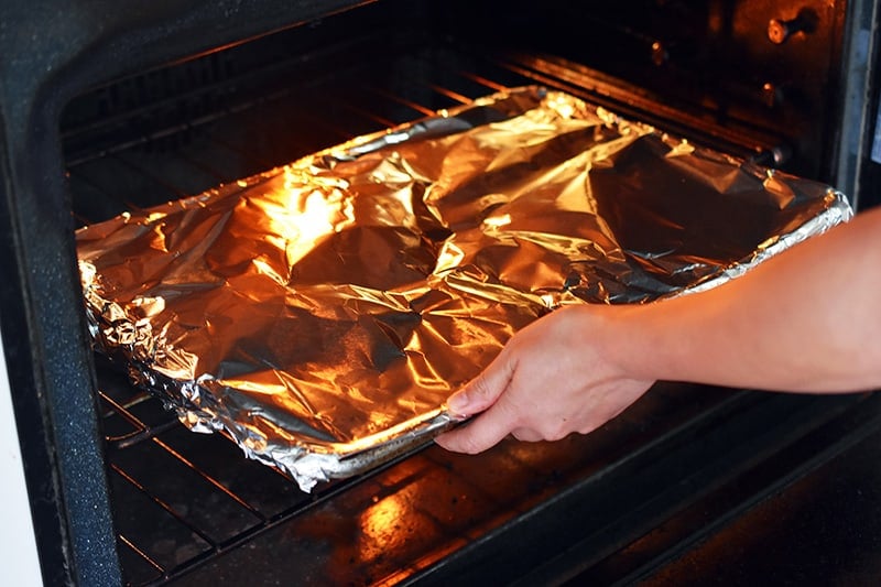 A foil-covered rimmed baking sheet is placed in the oven.