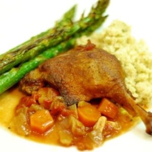 A plate containing braised duck leg, carrots, and asparagus.