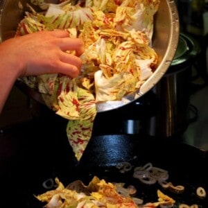 Someone is pouring chopped radicchio into a cast iron skillet to be stir fried.