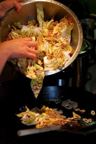 Someone is pouring chopped radicchio into a cast iron skillet to be stir fried.