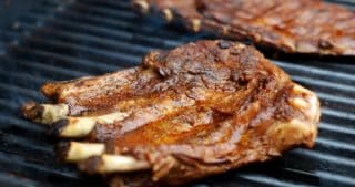 A close up of two racks of pork ribs searing on a hot grill.