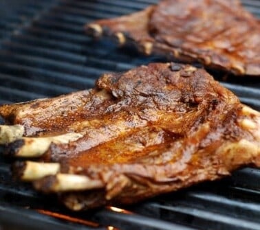 A close up of two racks of pork ribs searing on a hot grill.