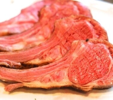 A rack of lamb cut into it's chops laying on a white plate.