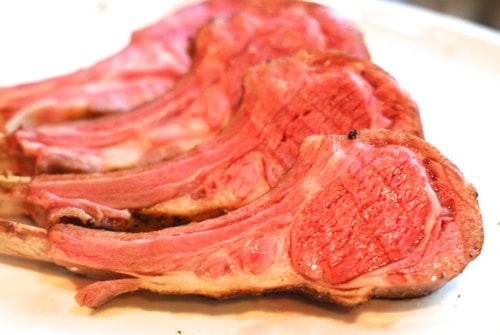 A rack of lamb cut into it's chops laying on a white plate.