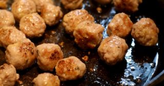 Paleo meatballs being pan fried in a cast iron skillet.
