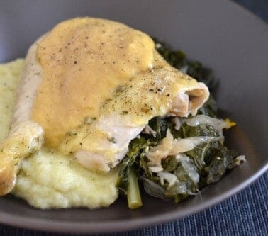 A shot of a chicken leg covered with gravy on a bed of mashed cauliflower and kale.
