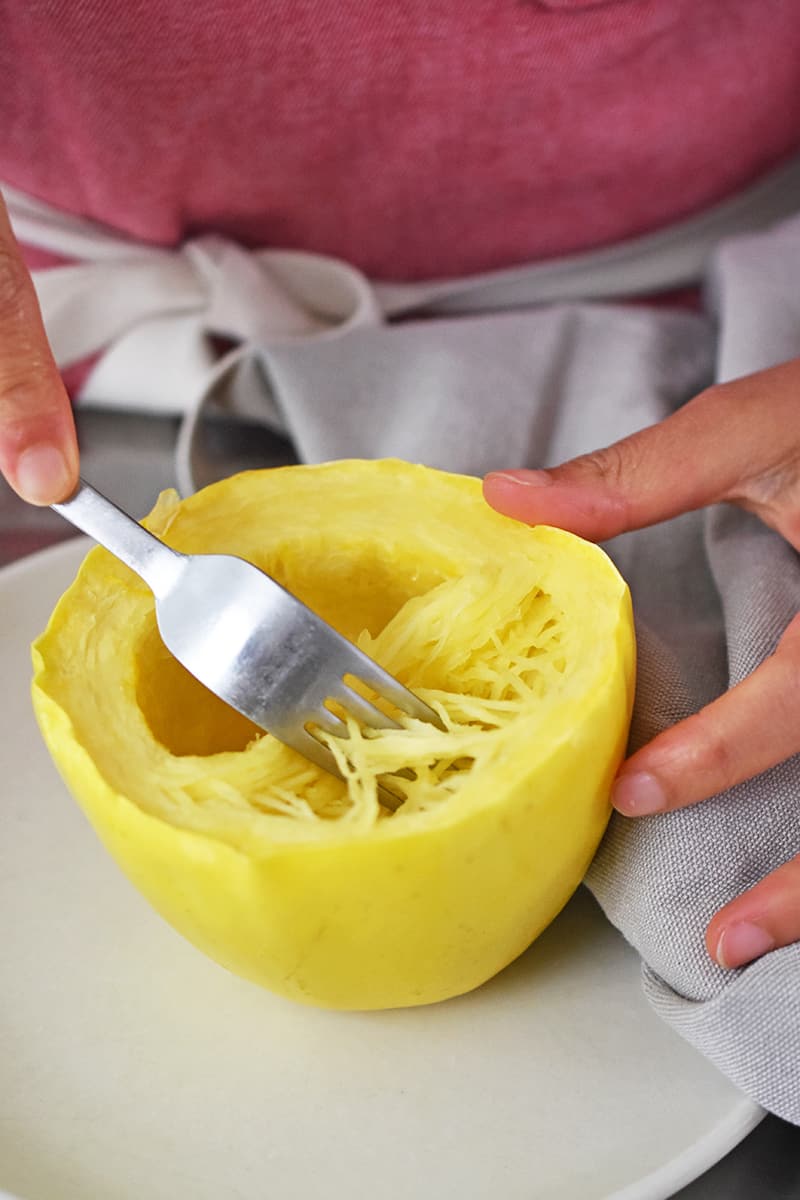 A fork is scraping the microwave spaghetti squash away from the skin.