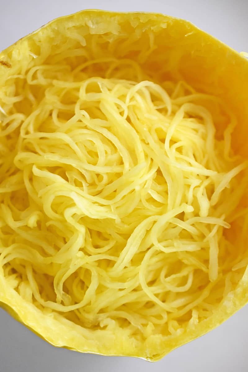 An overhead shot of a spaghetti squash cut in half crosswise with the cooked strands resembling long noodles.