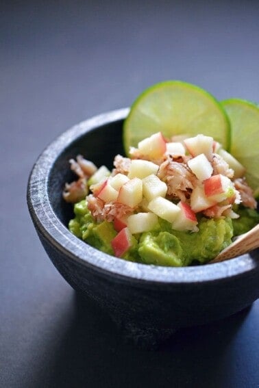Top view of guacamole topped with lump crab meat, diced apples, and lime slices.