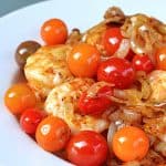 A plate of sautéed shrimp with roasted tomatoes and onions.