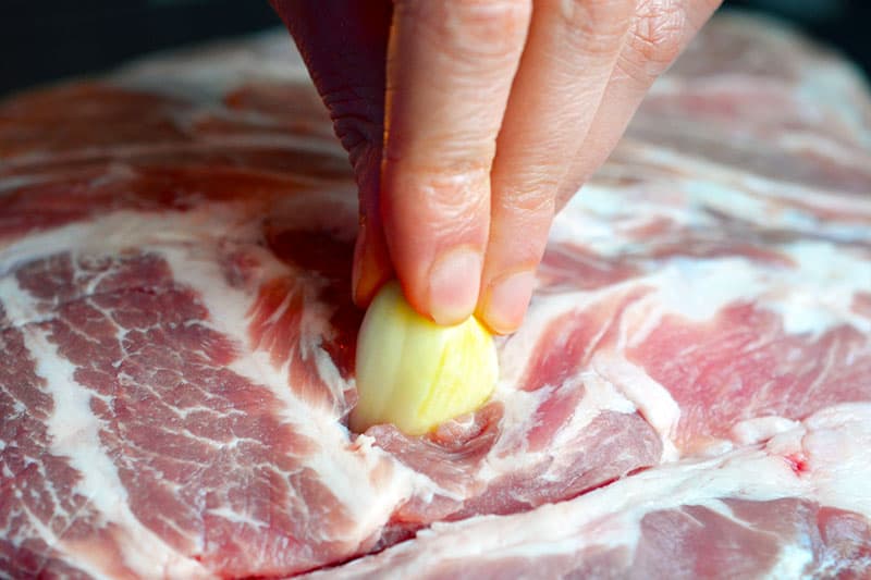 A closeup shot of inserting a whole garlic clove in a pork shoulder roast 