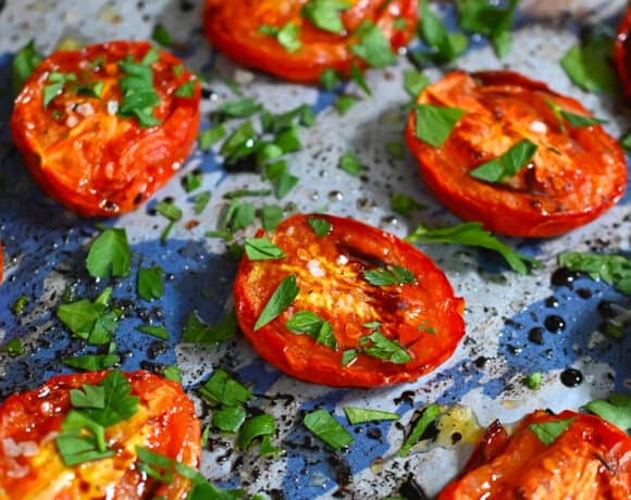 A closeup shot of oven roasted tomatoes on a blue baking sheet topped with chopped Italian parsley.