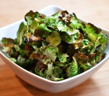 A square bowl is filled with crispy Brussels sprout chips, a paleo and vegan snack