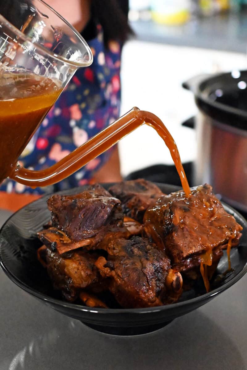 Pouring sauce from a fat separator onto a platter of braised Korean short ribs,