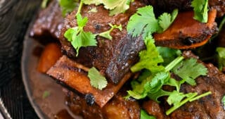 An bowl filled with braised Korean Short Ribs topped with cilantro in a black bowl.