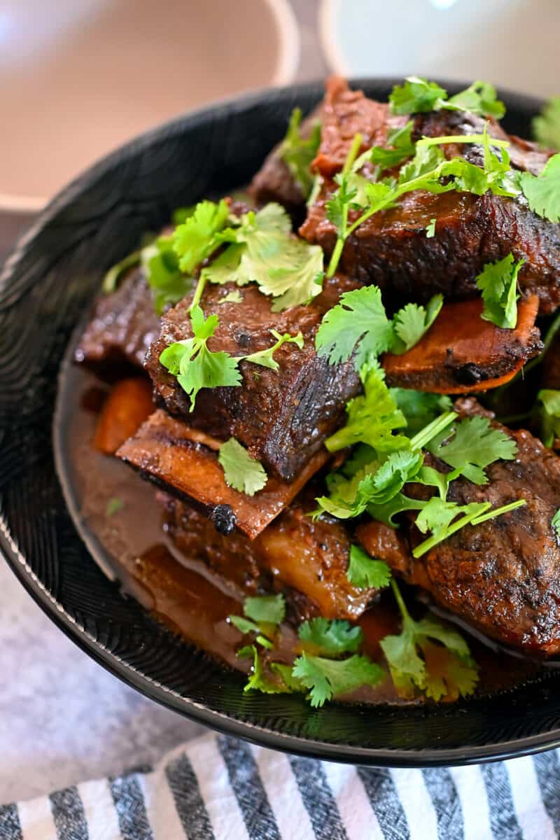 An bowl filled with braised Korean Short Ribs topped with cilantro in a black bowl.
