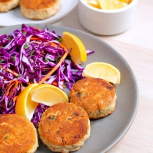 Two plates filled with paleo crab cakes, red cabbage slaw, and lemon wedges.