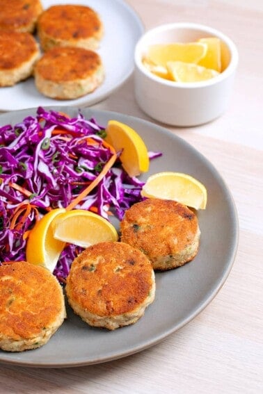 A plate filled with paleo crab cakes, red cabbage slaw, and lemon wedges.