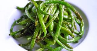 A closeup shot of roasted green beans in a white serving plate.
