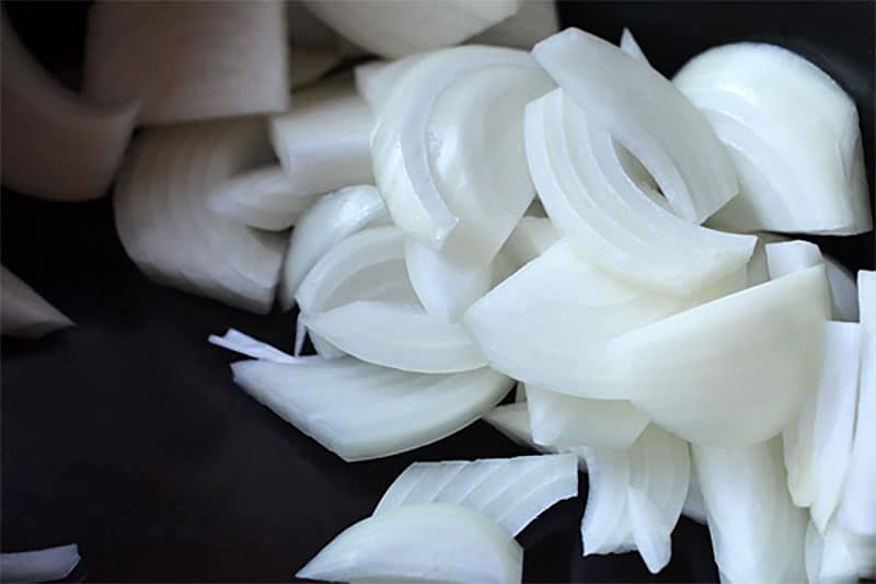 A shot of thinly sliced white onions on a black cutting board. They will be put into a Whole30-friendly Crock Pot Cheater Pork Stew by Michelle Tam / Nom Nom Paleo https://nomnompaleo.com