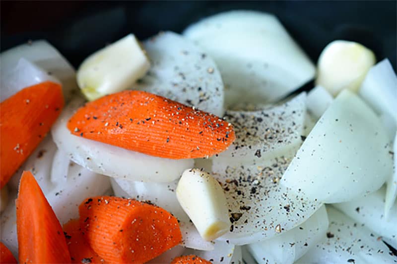 A closeup shot of the sliced vegetables seasoned with salt and pepper. They are the base of the Slow Cooker Cheater Pork Stew from Nom Nom Paleo.