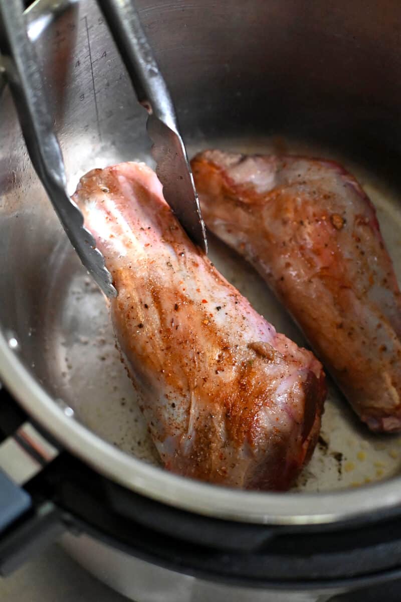 Closeup of a lamb shank being seared in an Instant Pot.