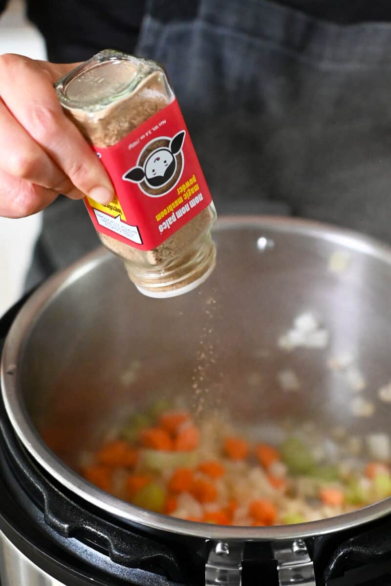 Seasoning chopped vegetables in an open Instant Pot with a bottle of Magic Mushroom Powder.