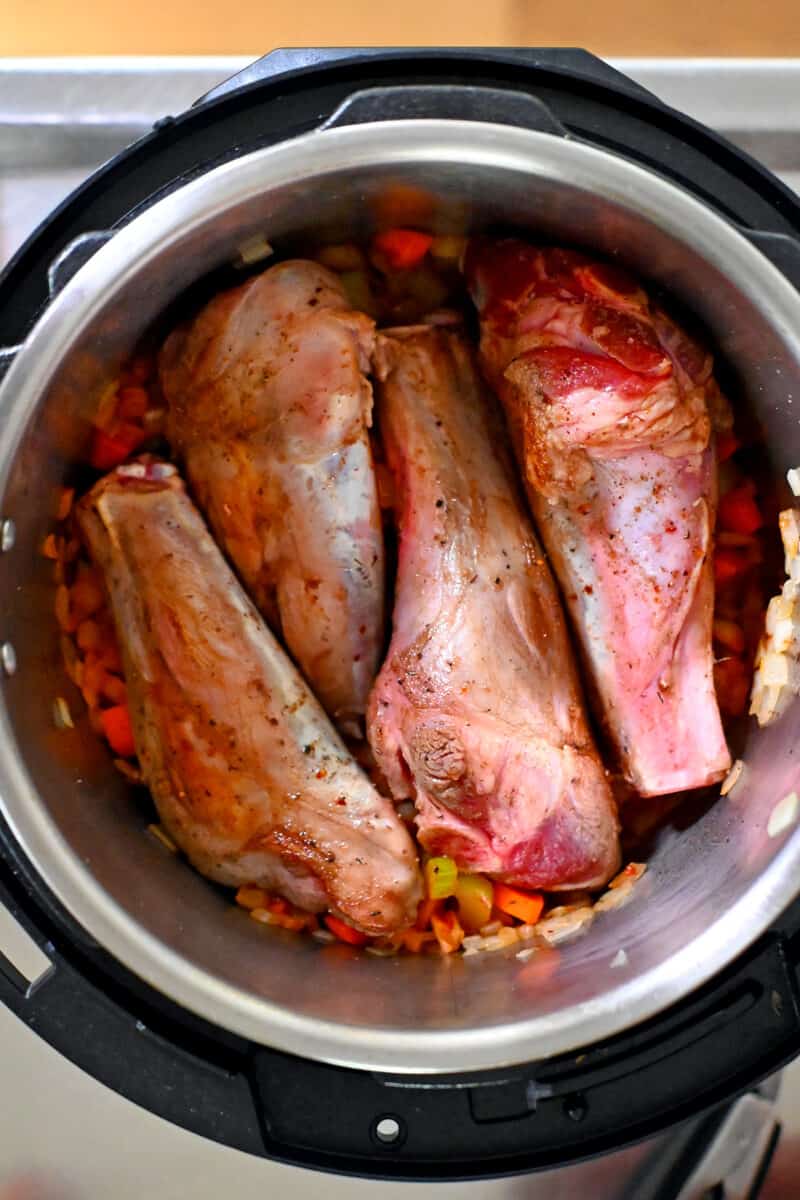 An overhead shot of an open Instant Pot with four seared lamb shanks on top of diced vegetables.