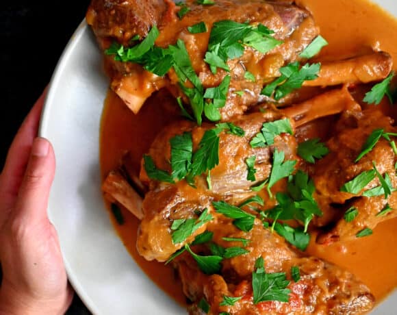 A hand holding a white plate with Instant Pot lamb chops ready to eat.