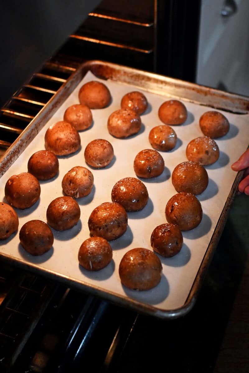 A baking sheet of cremini mushrooms (gill-side down) being placed into an oven.