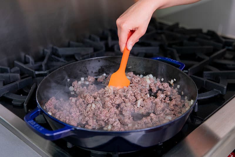 A cast iron skillet filled with cooked ground beef and diced onions.